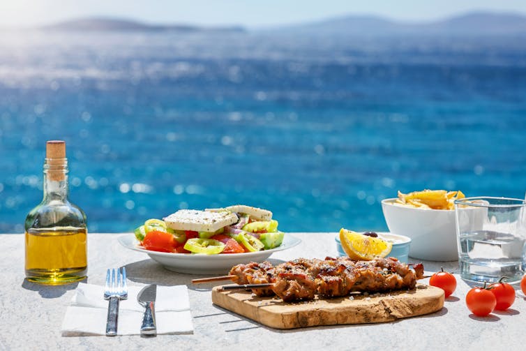 La diète méditerranéenne est en vogue, car elle représente ce que l'on a perdu 11 Une bouteille d’huile d’olive et des aliments santé sur une table, avec la mer en arrière-plan